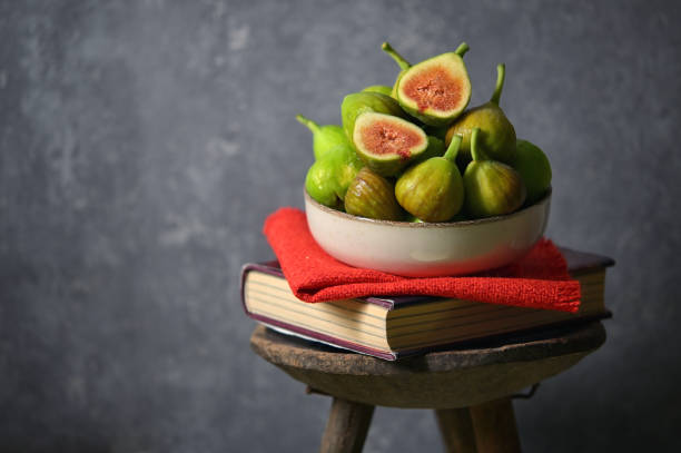 Ripe figs heap on book and old wooden stool in studio